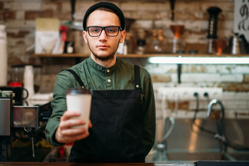 Image: A young man serving a flat white coffee in a cafe. 