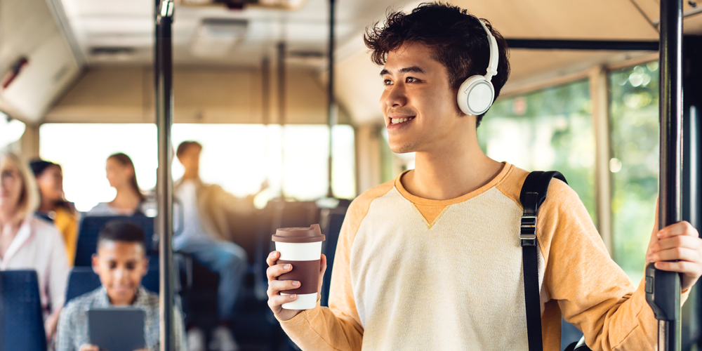 A young man on the bus, listening to music and holding a take-away coffee.